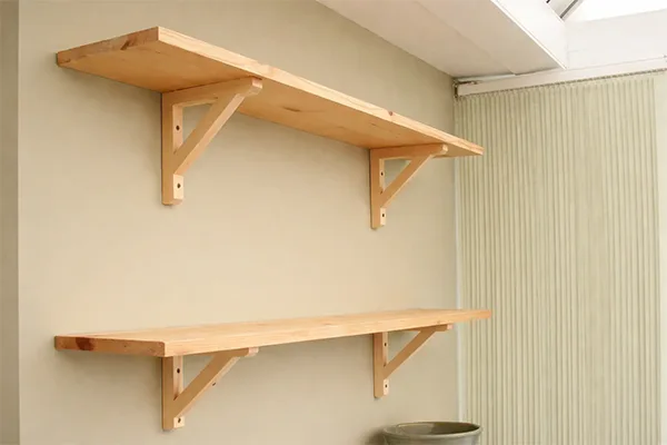 Photographie montrant deux étagères murales simples en bois clair fixées par des équerres.