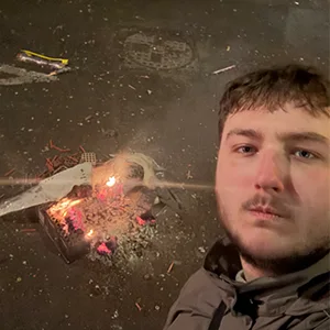 Photographie montrant Keelan Bierlier en extérieur de nuit avec un petit feu en arrière-plan.